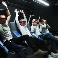 Dzieci w 7D kinie z okularami 3D, z rękami w górze, przeżywają emocje podczas seansu.