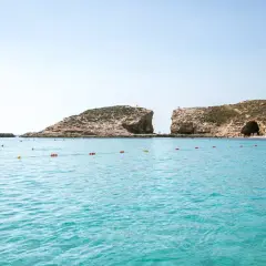 Turkusowa woda, skaliste klify i plaża z ludźmi. Idealne miejsce na wakacje, zastanawiasz się, ile leci się na Maltę?