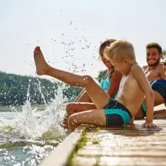Rodzina ciesząca się latem nad jeziorem, dzieci chlapią wodą.