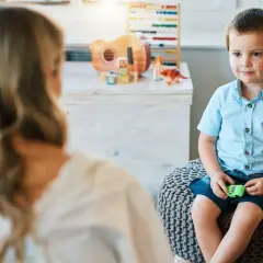 Chłopiec z afazją siedzi na pufie, rozmawiając z terapeutką. Czy dziecku z afazją przysługuje zasiłek pielęgnacyjny?