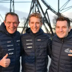 Trzech mężczyzn w kurtkach z logo Energylandii pozuje na tle konstrukcji roller coastera.