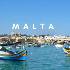 Malta maj: kolorowe łodzie luzzu kołyszą się na lazurowej wodzie, w tle malownicze miasteczko z kopułami kościołów.