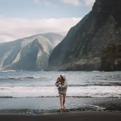 Matka z dzieckiem na plaży na Maderze, w tle góry i ocean.