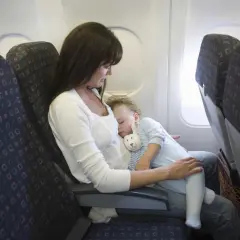Kobieta trzyma śpiące dziecko na kolanach w samolocie.