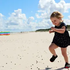 Radosna wycieczka dla dzieci na plażę. Mała dziewczynka w letniej sukience biega po piasku, ciesząc się słońcem i chmurami.