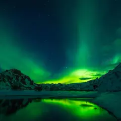 Reykjavik zorza polarna kiedy? Zielone światła tańczą nad ośnieżonymi górami i spokojną wodą.