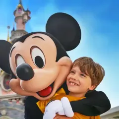 Chłopiec przytula się do Myszki Miki na tle zamku w Disneylandzie.