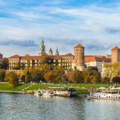 Wawel zwiedzanie z przewodnikiem. Widok na zamek i Wisłę z łodziami w jesiennej scenerii.