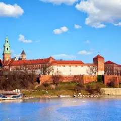 Majestatyczny Wawel góruje nad Wisłą. Widok na wejście na Wawel z rzeki, z widoczną barką i błękitnym niebem.