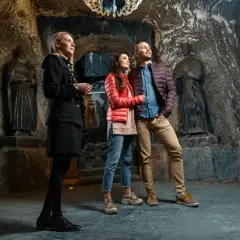 Przewodniczka oprowadza parę po kopalni soli w Wieliczce. Trasa turystyczna zachwyca rzeźbami i surowym pięknem.