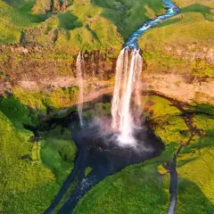 Wspaniały wodospad na Islandii latem. Zielone wzgórza i rwąca rzeka tworzą malowniczy krajobraz. Idealne miejsce, by zobaczyć, co Islandia ma do zaoferowania.