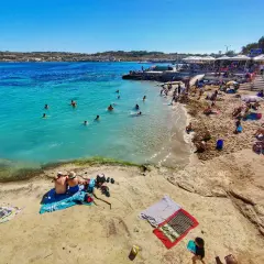 Słoneczna plaża na Malcie w październiku. Ludzie kąpią się w turkusowej wodzie i opalają na piasku. Czy warto? Zdecydowanie tak!