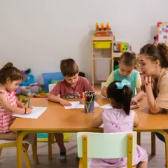 Nauczycielka z dziećmi przy stole, rysują kredkami. Czy taki facet z dzieckiem to ma sens? Tak, to sensowne i piękne!
