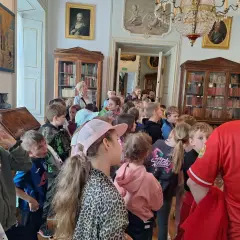 Wycieczka szkolna w Pałacu w Nieborowie. Dzieci słuchają przewodnika wśród zabytkowych mebli i obrazów.