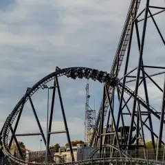 Pasażerowie Hyperion roller coaster pędzą po stalowej konstrukcji, chmury na niebie dodają dramatyzmu.