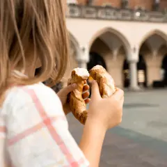 Dziecko trzyma obwarzanka na tle Sukiennic. Smaki Krakowa z dzieckiem.