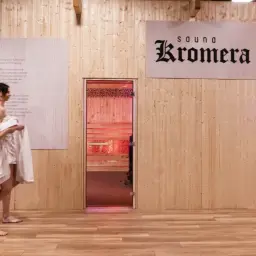Dwie kobiety w ręcznikach wchodzą do strefy nietekstylnej, gdzie znajdują się sauny z podświetlanymi drzwiami.