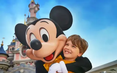 Chłopiec przytula się do Myszki Miki na tle zamku w Disneylandzie.