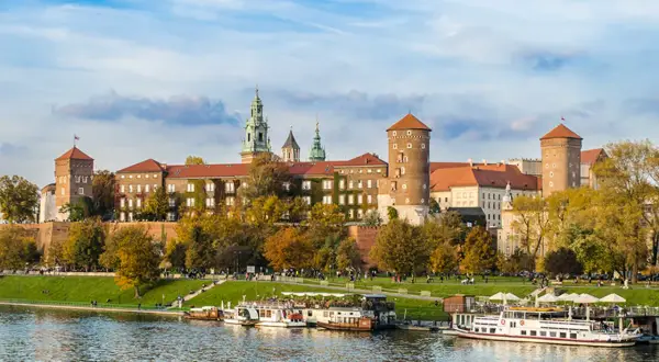 Wawel zwiedzanie z przewodnikiem. Widok na zamek i Wisłę z łodziami w jesiennej scenerii.