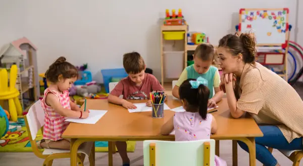 Nauczycielka z dziećmi przy stole, rysują kredkami. Czy taki facet z dzieckiem to ma sens? Tak, to sensowne i piękne!
