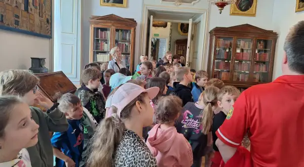 Wycieczka szkolna w Pałacu w Nieborowie. Dzieci słuchają przewodnika wśród zabytkowych mebli i obrazów.