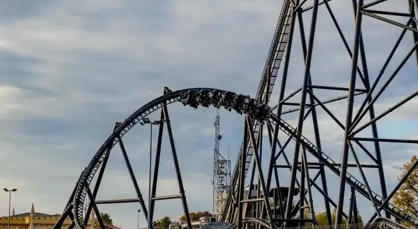 Pasażerowie Hyperion roller coaster pędzą po stalowej konstrukcji, chmury na niebie dodają dramatyzmu.