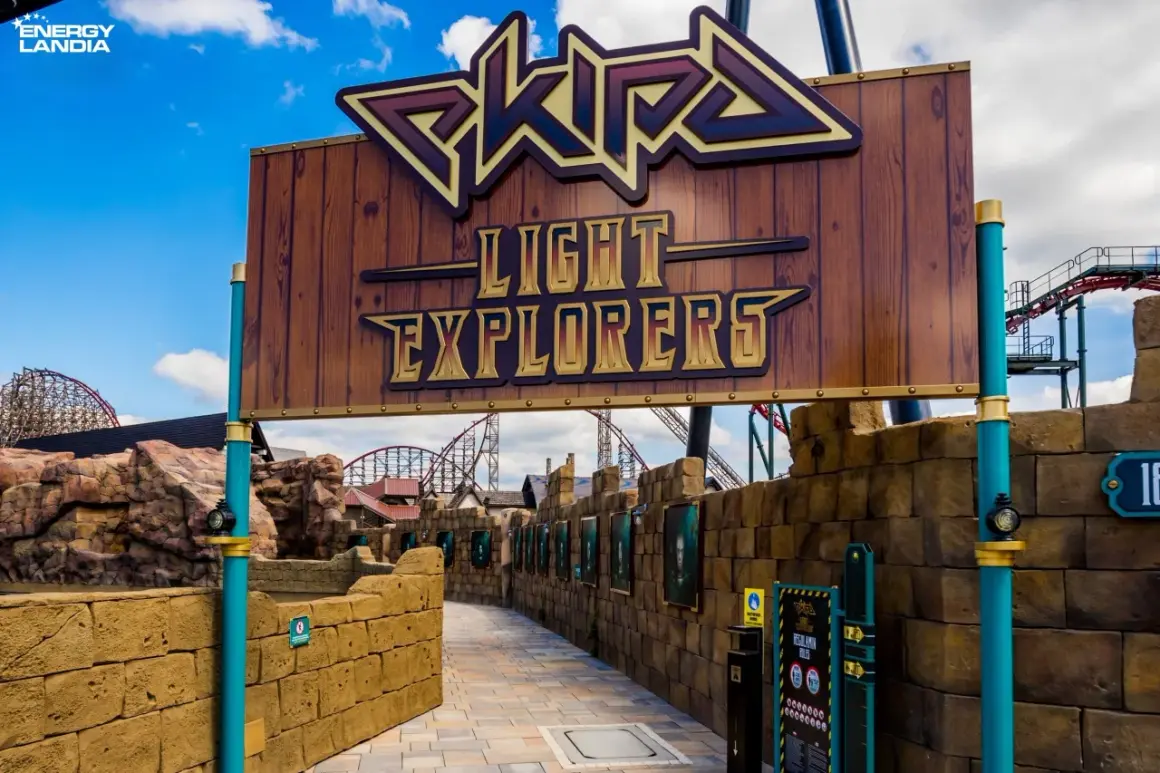 Wejście do ekipy rollercoaster "Light Explorers" w Energylandii. Drewniany szyld z napisem i widokiem na tor kolejki górskiej.