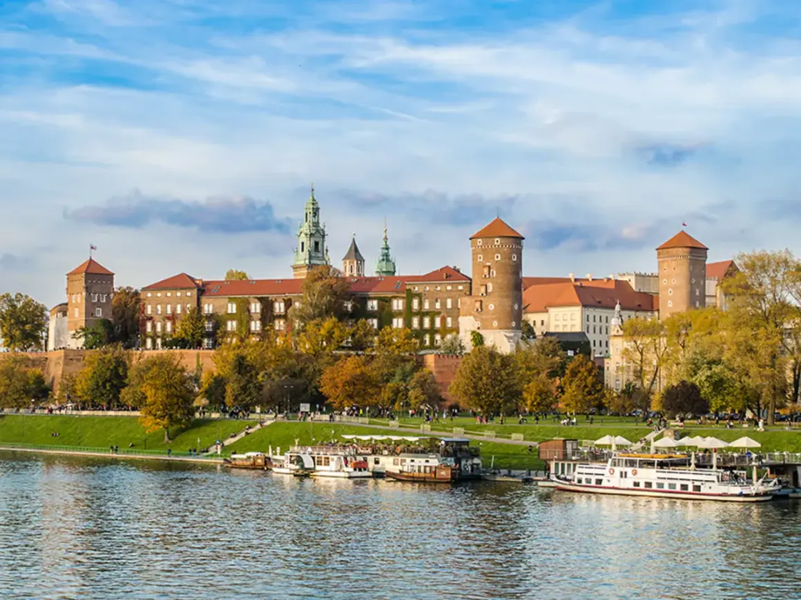 Wawel zwiedzanie z przewodnikiem. Widok na zamek i Wisłę z łodziami w jesiennej scenerii.