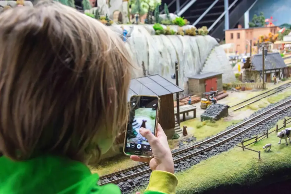 Dziecko fotografuje telefonem miniaturową wioskę w parku miniatur Wrocław.