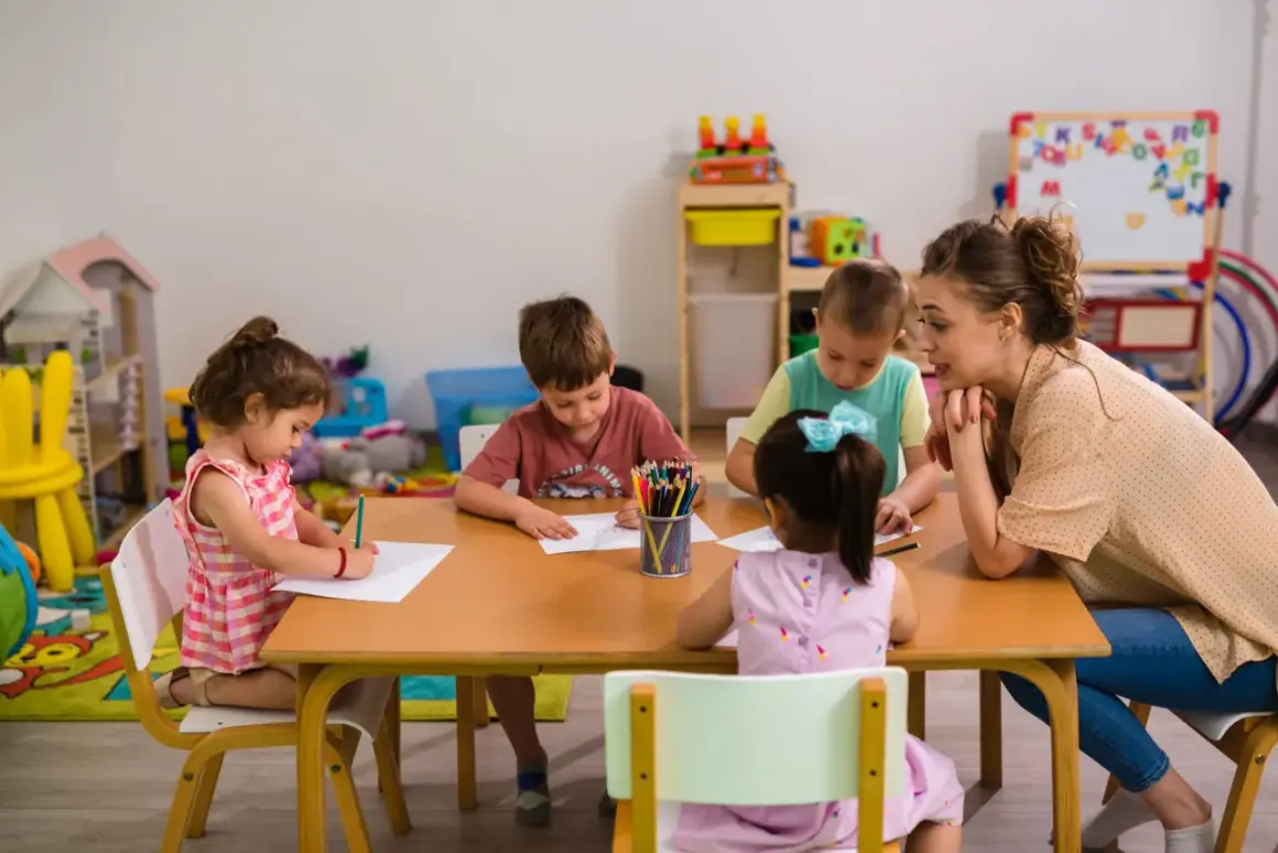 Nauczycielka z dziećmi przy stole, rysują kredkami. Czy taki facet z dzieckiem to ma sens? Tak, to sensowne i piękne!