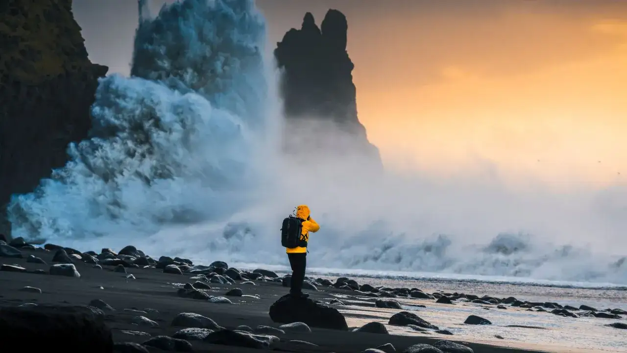 Osoba w żółtej kurtce podziwia potężne fale rozbijające się o czarną plażę. Islandia najpiękniejsze miejsca w całej okazałości.