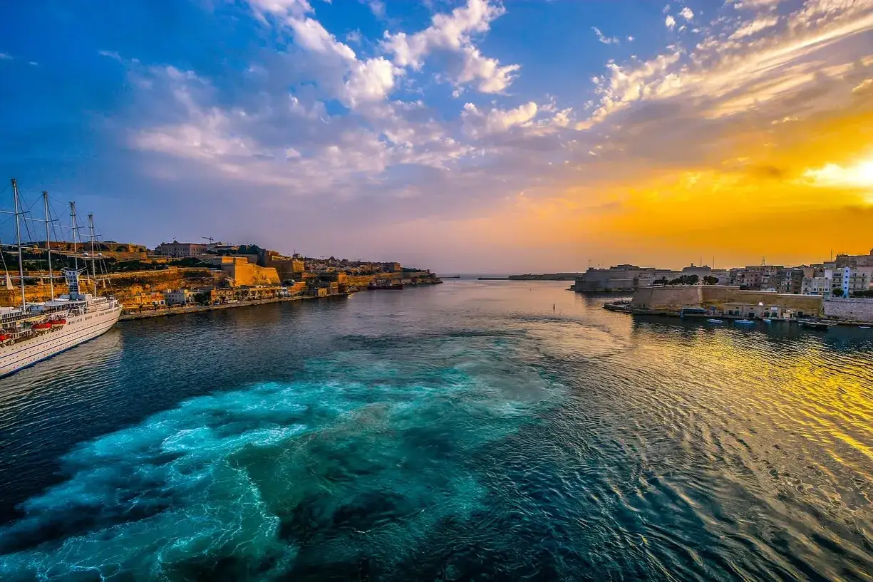 Malta zachód słońca nad portem, z białym żaglowcem i turkusową wodą.