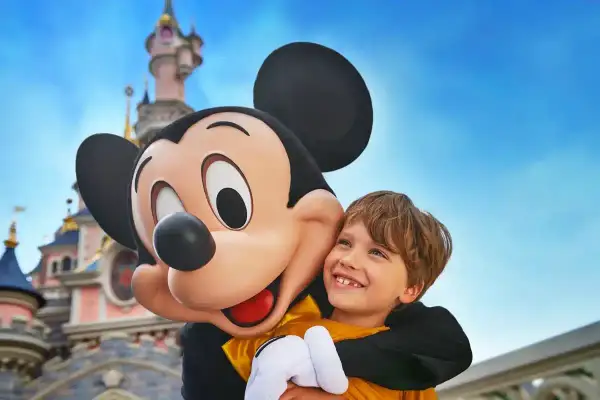 Chłopiec przytula się do Myszki Miki na tle zamku w Disneylandzie.